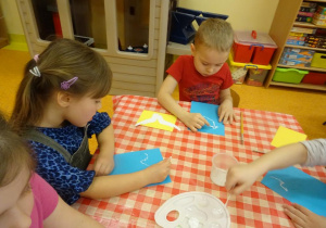 Dzieci stemplują patyczkami białą farbą gołąbka.